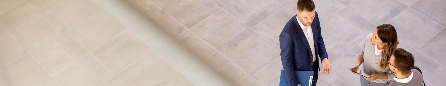 Three business professionals engaged in conversation in a modern lobby setting.