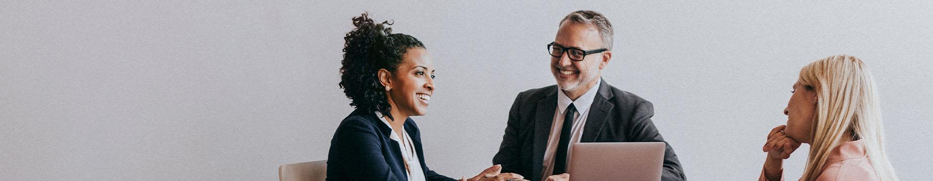 Two business professionals engaged in discussion at a table, with a laptop open between them.