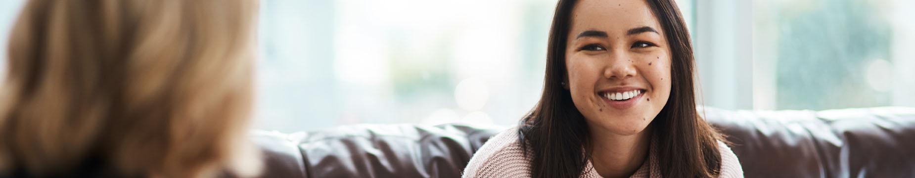 A woman sitting on a couch, smiling warmly, exuding a sense of comfort and happiness in her relaxed environment.