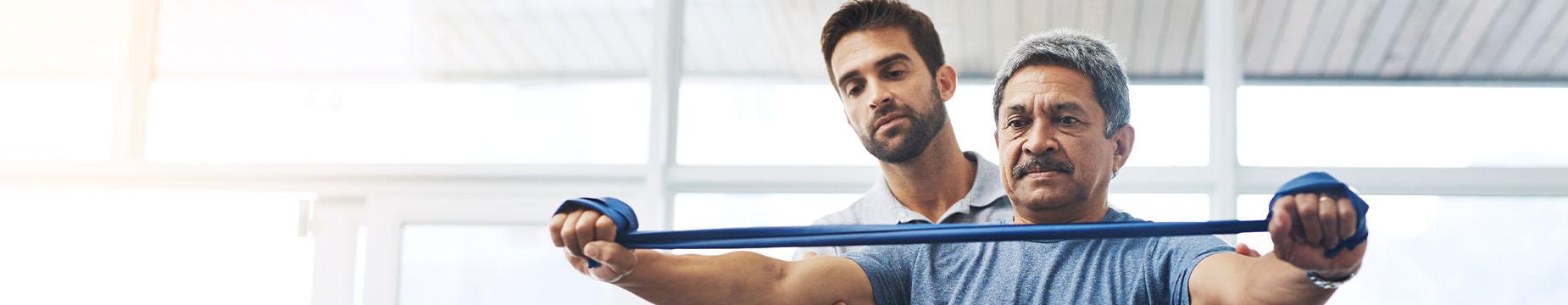 A man performs exercises in the foreground, while another man is visible in the background, observing the activity.