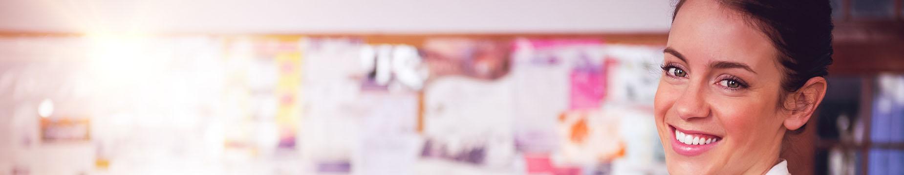 A smiling woman stands in a classroom, holding a folder, exuding a sense of positivity and engagement in her environment.