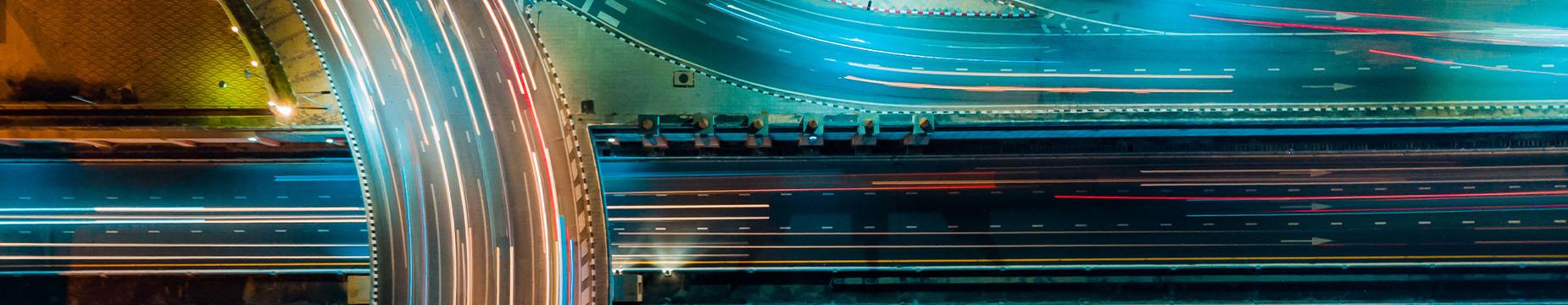 Aerial view of a highway illuminated at night, showcasing flowing traffic and city lights in the surrounding area.