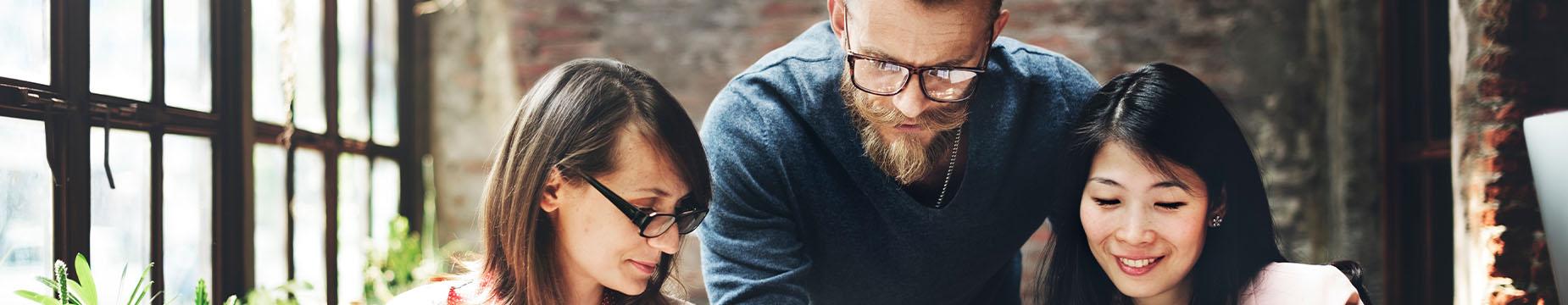 A man and two women are gathered around a laptop, engaged in discussion and sharing ideas.