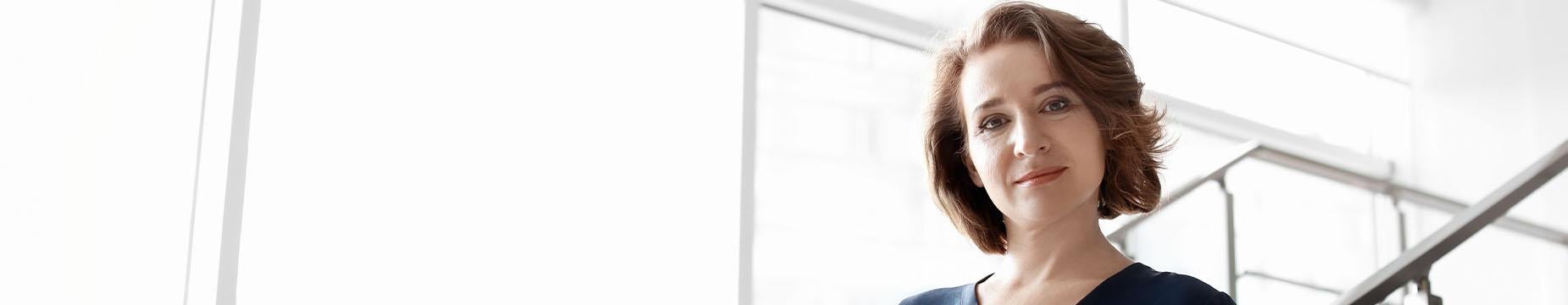 A professional woman in a business suit confidently holds a folder, embodying a poised and determined demeanour.