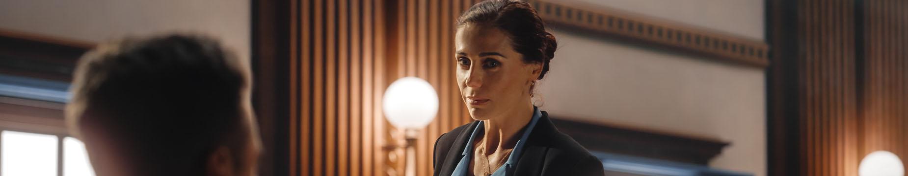 A woman in a suit and tie stands confidently in a courtroom, embodying professionalism and authority.
