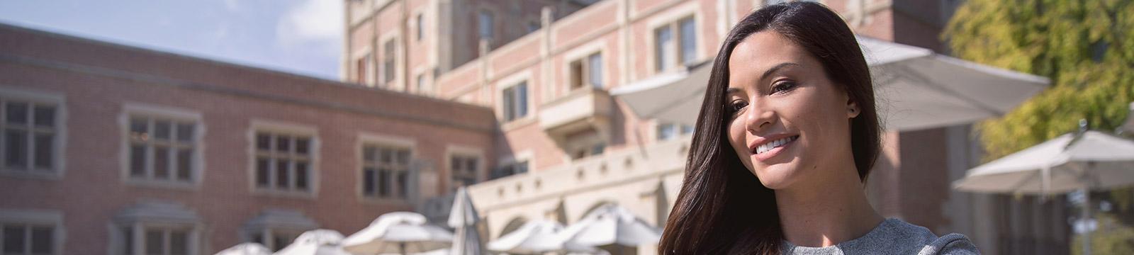 A woman smiles brightly while standing in front of a modern building, showcasing a sense of joy and confidence.