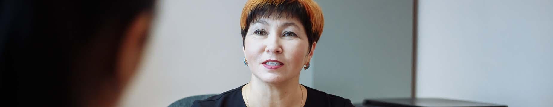 A female principal seated at a table, extending her hands outward in a welcoming gesture.
