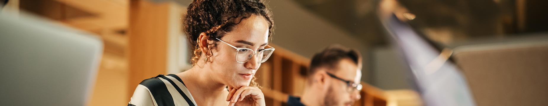 A woman and a man are seated at a table, each using their laptops, engaged in a collaborative work session.