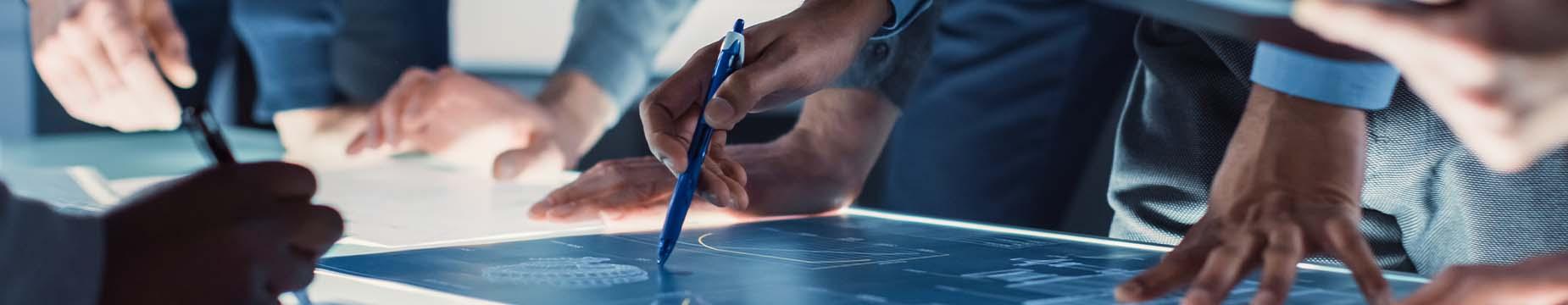 Individuals collaborating on a blueprint, using pens to make detailed annotations and adjustments to the design.