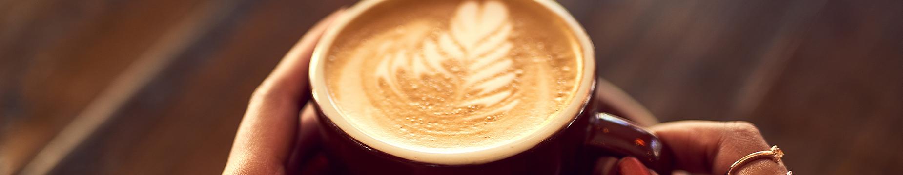 A woman's hands gently cradle a steaming cup of coffee, showcasing warmth and comfort in a cozy setting.
