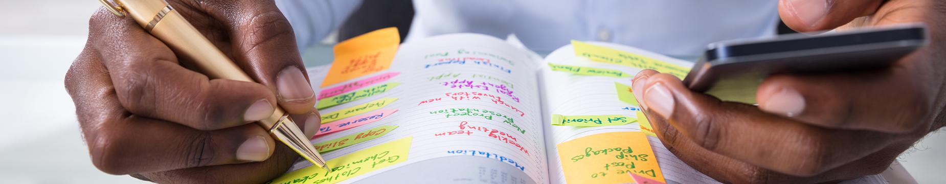 A man diligently writing in a book, focused on his task with a pen in hand and pages open before him.