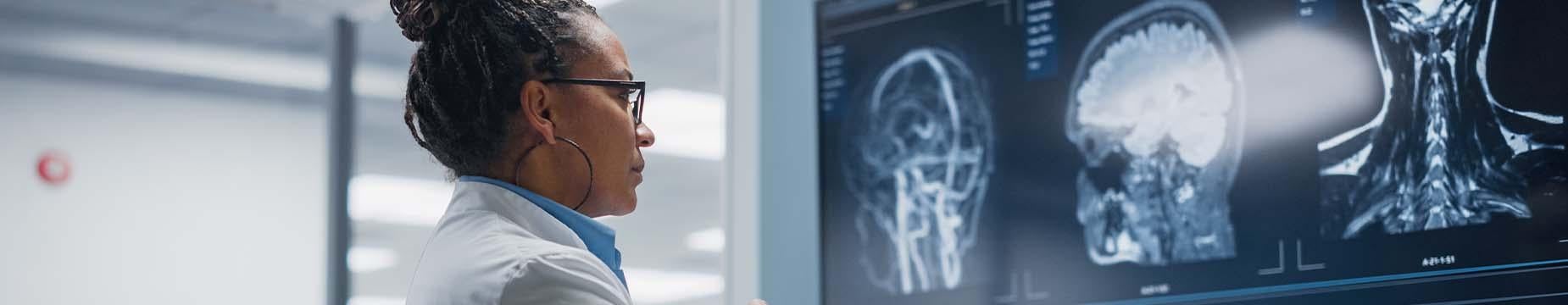 A woman in a lab coat examines data displayed on a computer screen in a laboratory setting.