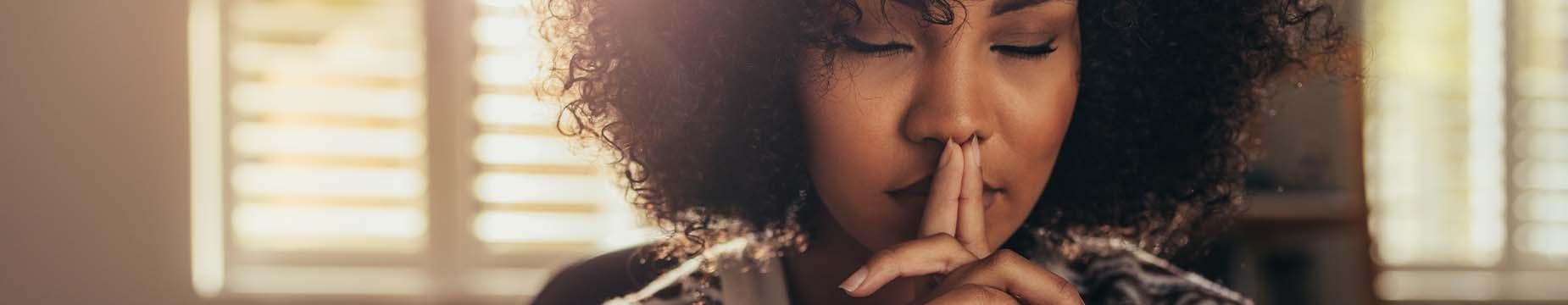 A woman with her hand on her mouth and a finger to her lips, signalling for silence or contemplation.
