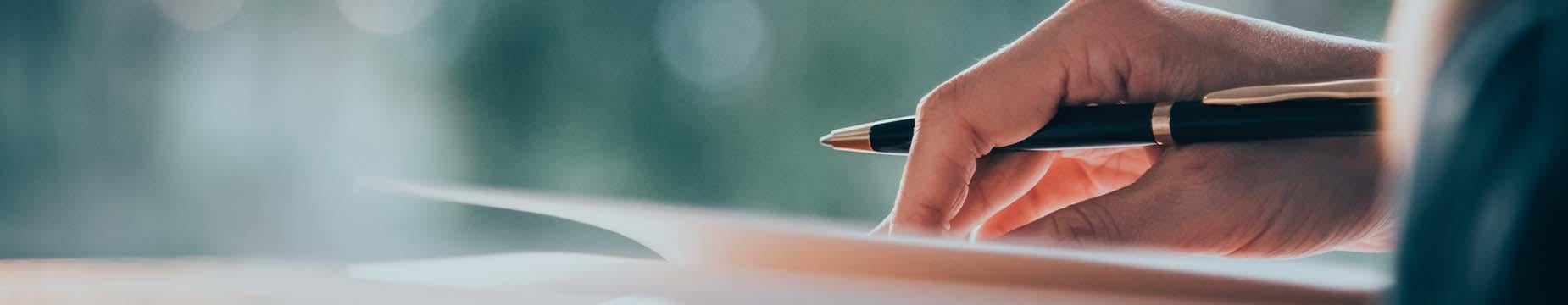 A person writing on paper with a pen, focused on their task, showcasing the act of note-taking or drafting.