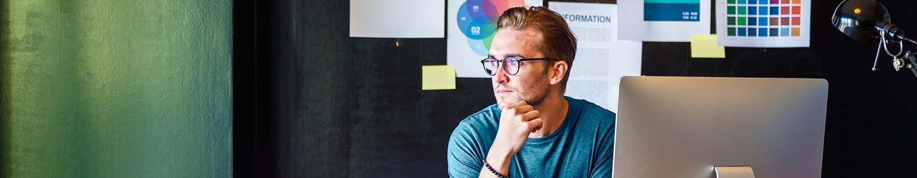 A man seated at a desk, working on a laptop and a desktop computer, focused on his tasks.