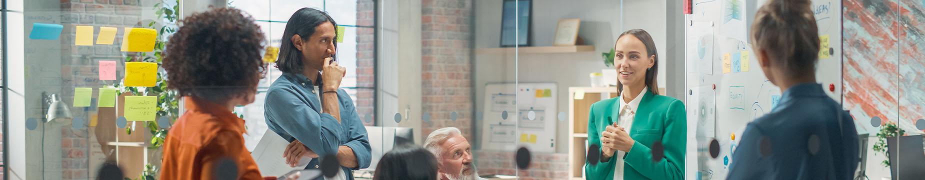 A diverse group of professionals collaborates in an office, surrounded by colorful sticky notes on the wall.