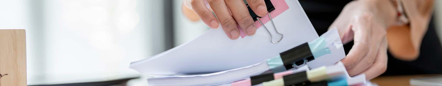 A person holds a neatly organized stack of papers secured with a clip, showcasing a professional and tidy appearance.