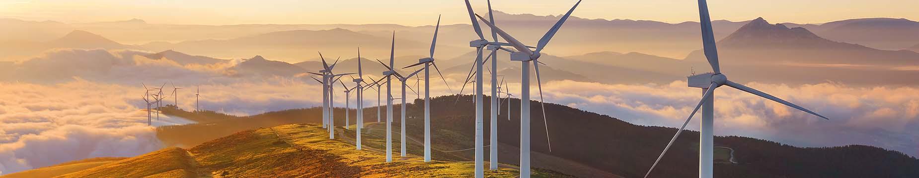 Wind turbines atop a mountain, surrounded by clouds, showcasing renewable energy in a scenic landscape.