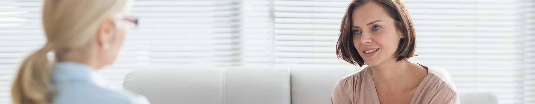 A woman engages in conversation with another woman while seated on a couch, showcasing a moment of connection and dialogue.