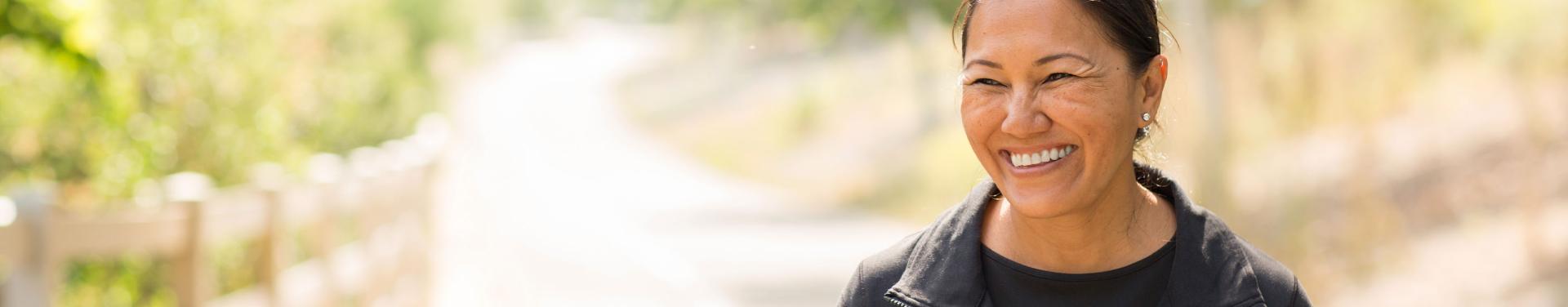 A smiling woman stands in front of a softly blurred background, radiating joy and warmth.