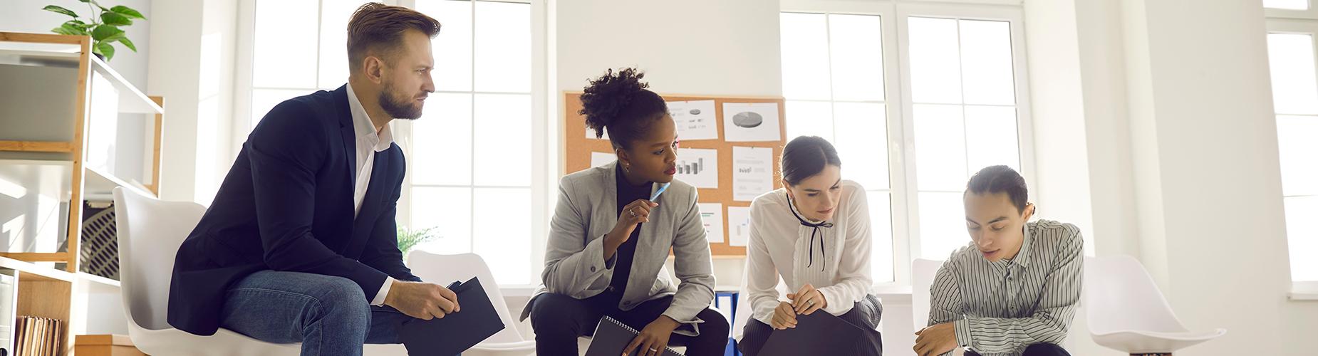 A diverse group of individuals gathered in a room, focused on a laptop placed on a table in front of them.