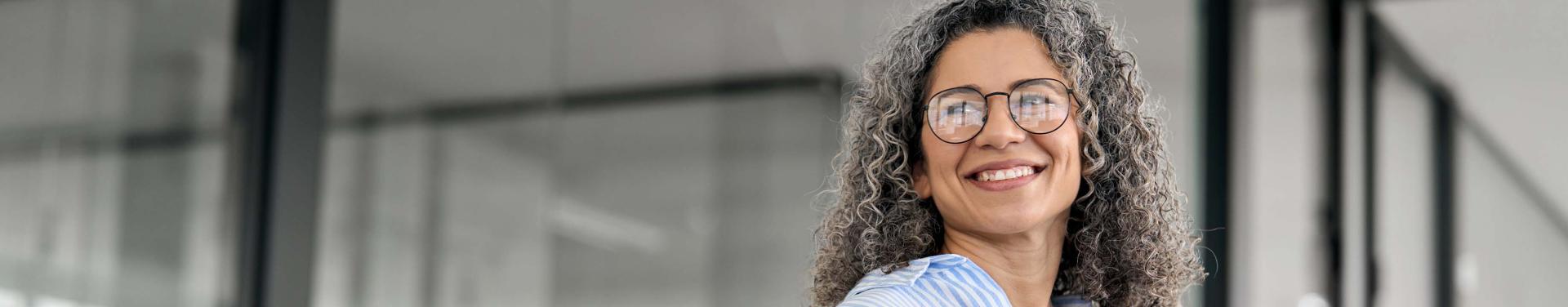 A woman wearing glasses smiles while holding a tablet computer in her hands, engaged in her digital world.