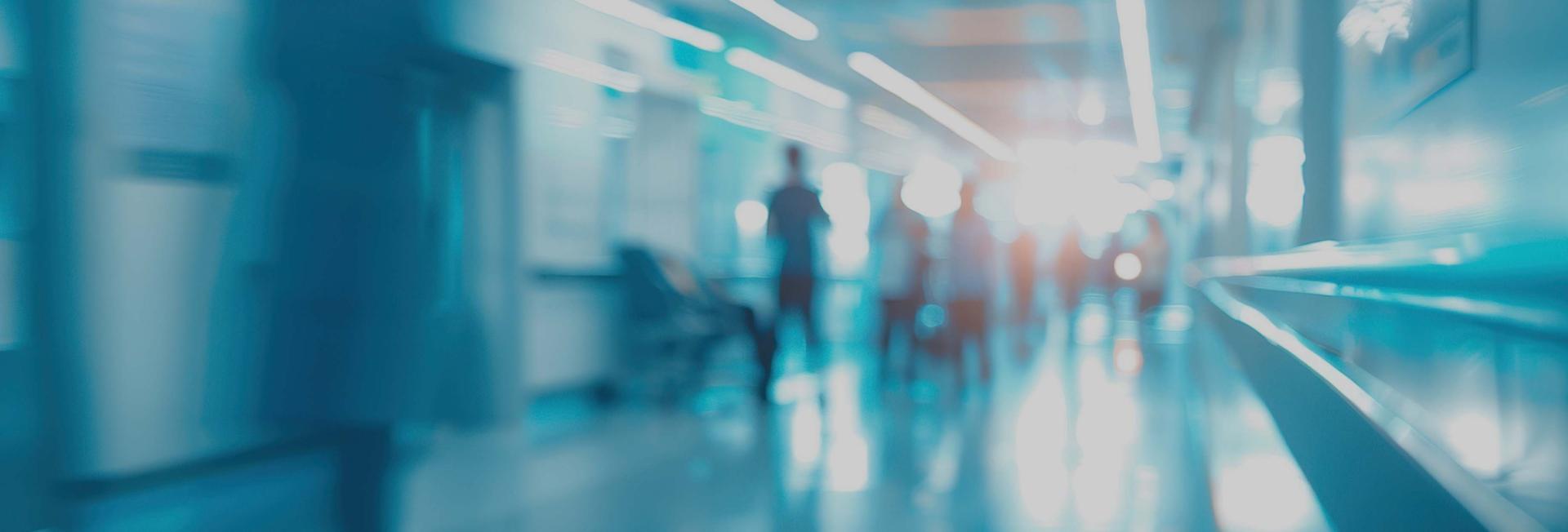 A blurred hallway scene featuring individuals walking, creating a sense of movement and depth in the space.