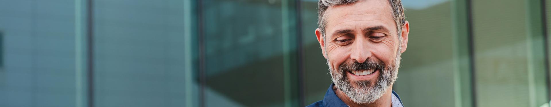 A bearded man in a blue shirt is holding a cell phone, looking engaged and focused on the screen.