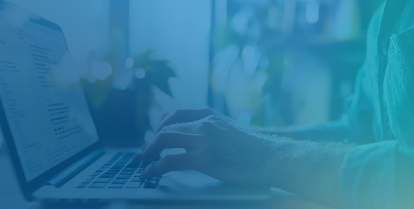 A person focused on typing on a laptop computer, with hands positioned on the keyboard and screen illuminated.