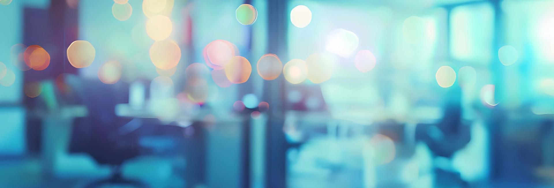 Blurred image depicting a room filled with individuals seated at various tables, creating a lively atmosphere.