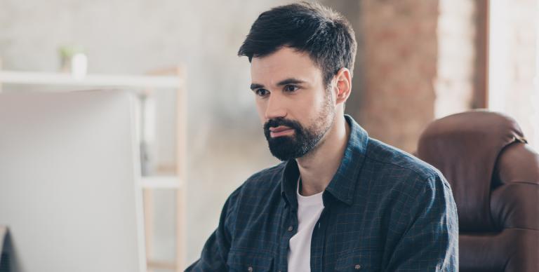 A bearded man seated at a desk, focused on his work in front of a computer screen.