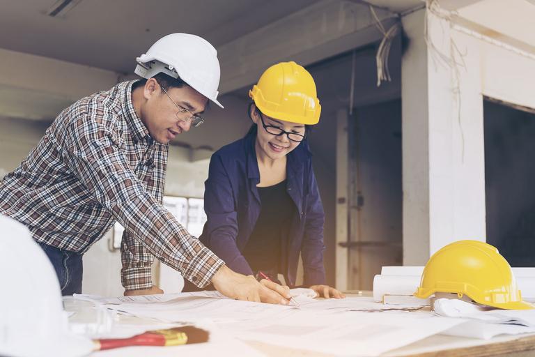 Two individuals in hard hats collaborating on construction plans at a worksite, focused on their project.