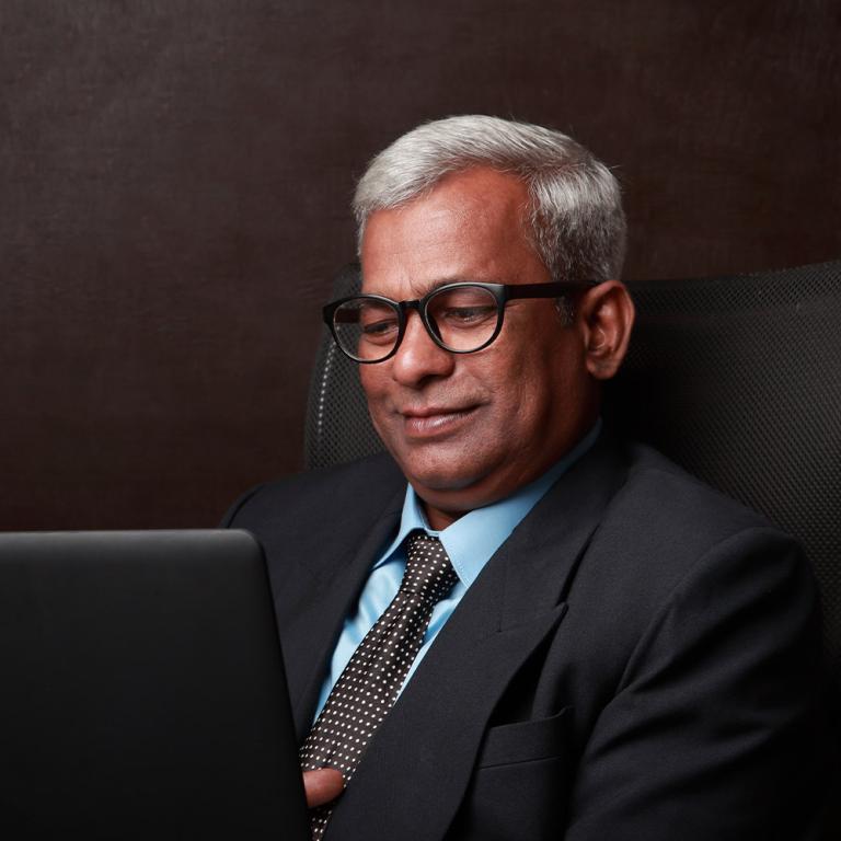 A male MBA student in a suit and tie seated in a chair, focused on his laptop, exuding professionalism and concentration