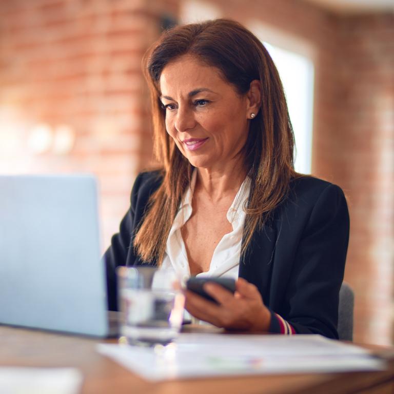 A professional female MBA accounting student in a business suit is focused on her laptop, engaged in work or a virtual meeting