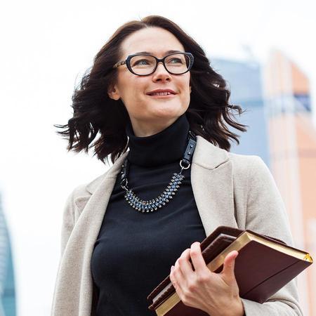 A female business law student wearing glasses smiles while holding a book, exuding joy and enthusiasm