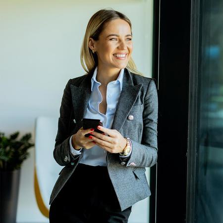 A professional female student in a business suit is holding her cell phone, appearing engaged in a conversation