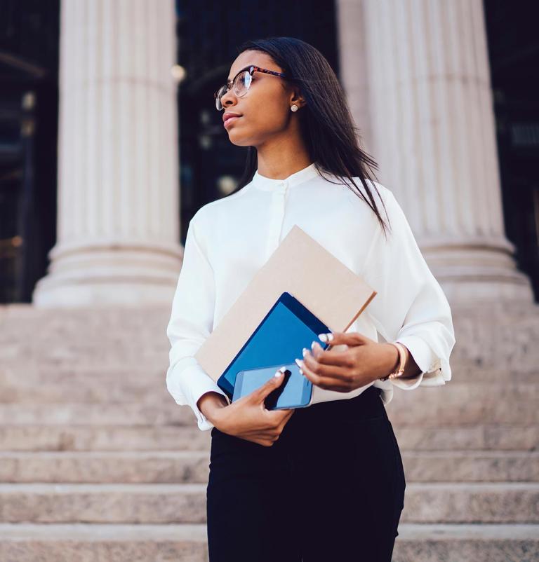 A female law student wearing glasses is holding a folder, appearing focused and engaged in her work or study