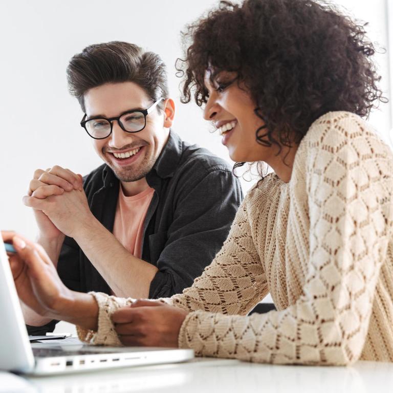  A man and woman share a joyful moment, smiling as they look at a laptop, highlighting their connection and interest in the screen.