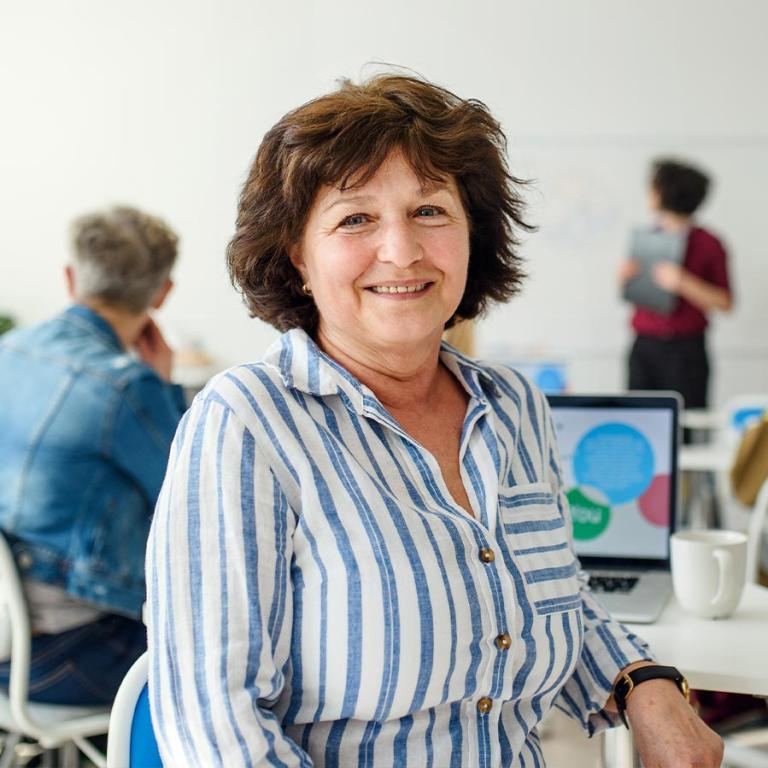 A woman seated at a table in an office, engaged in work with a focused expression and a laptop in front of her.