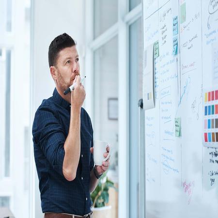 Male Engineering student standing in front of a whiteboard with marker in hand deep in thought