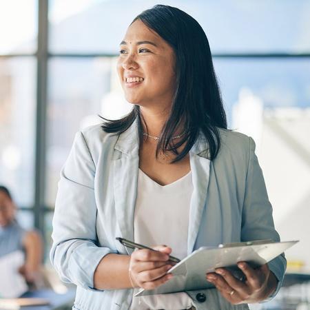 A female business student smiles confidently while holding a clipboard, exuding professionalism and positivity.