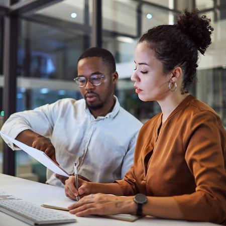 A business student at work collaborating with a colleague in a modern office, focused on their work and sharing ideas