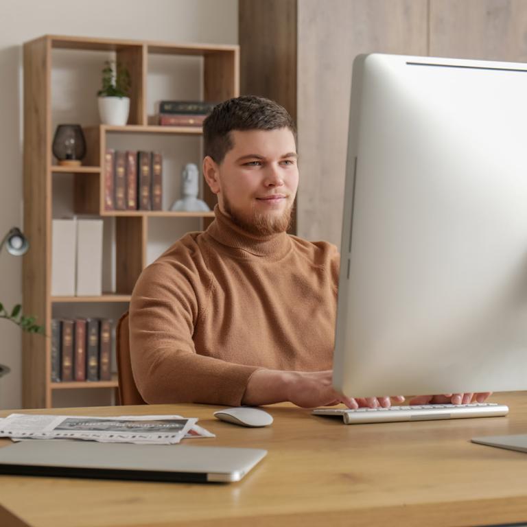 A man in a brown sweater sits at a desk, focused on his computer, creating a productive work environment.