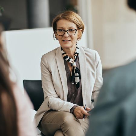 A female mental health student wearing glasses engages in conversation with a group of people, showcasing an interactive discussion