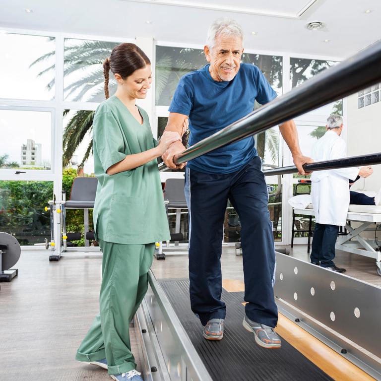 A man performs exercises in the foreground, while woman is visible in the background, observing the activity.