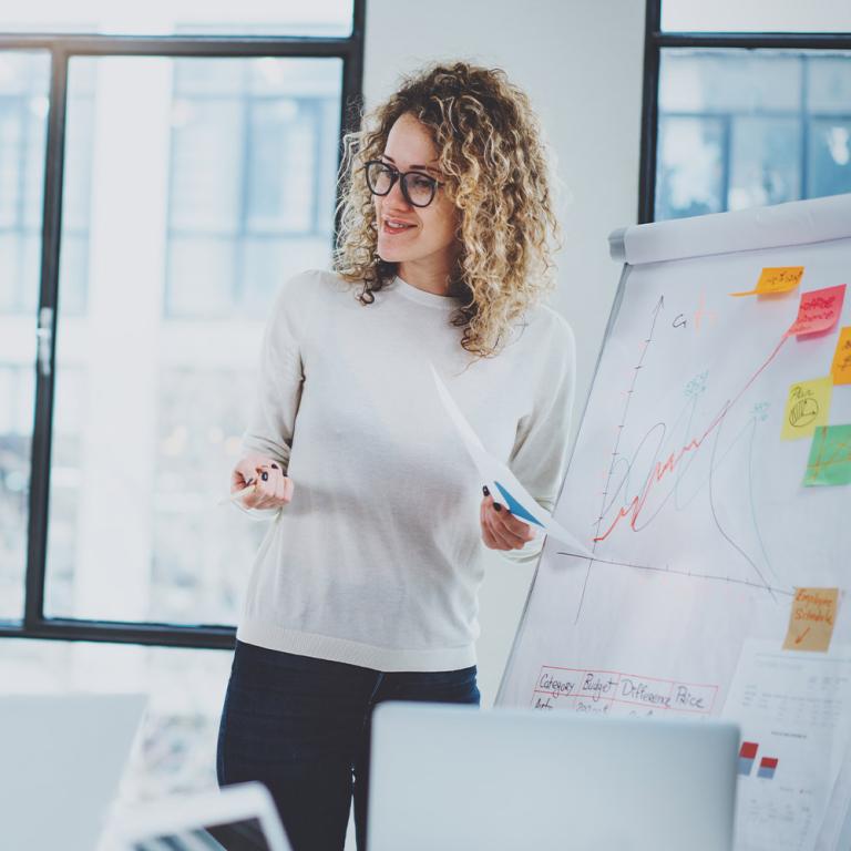A female project management student stands confidently in front of a whiteboard, ready to present her ideas and engage with her audience