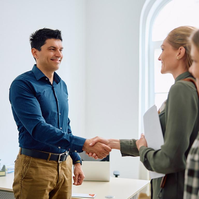 A man shakes hands with two women in a professional office setting, symbolising collaboration and agreement.