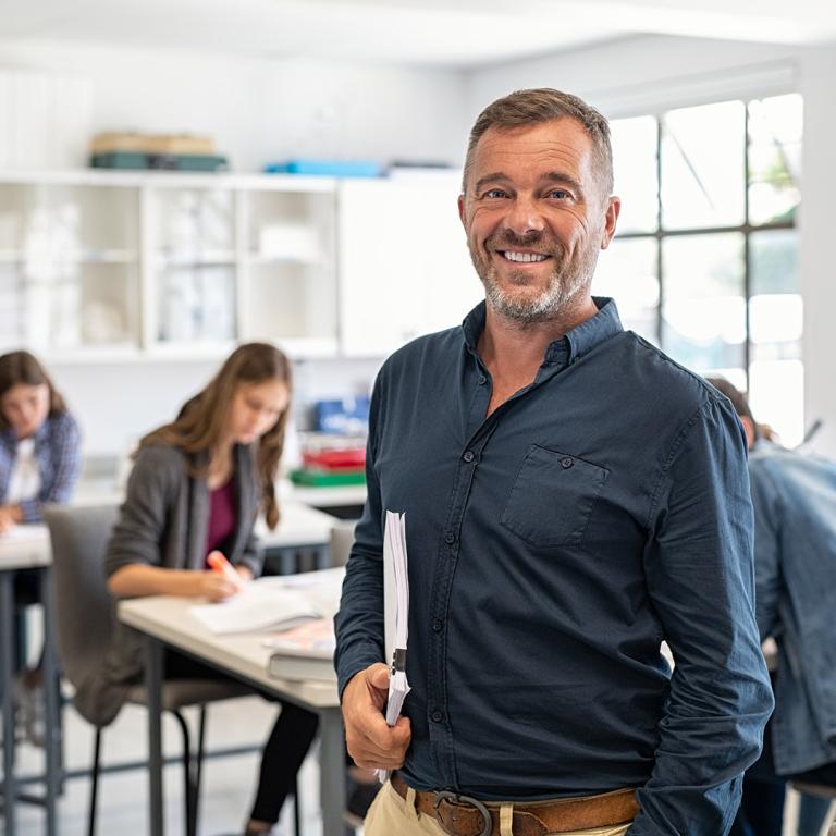 A man stands in front of a classroom, engaging with students seated at their desks, fostering a learning environment.