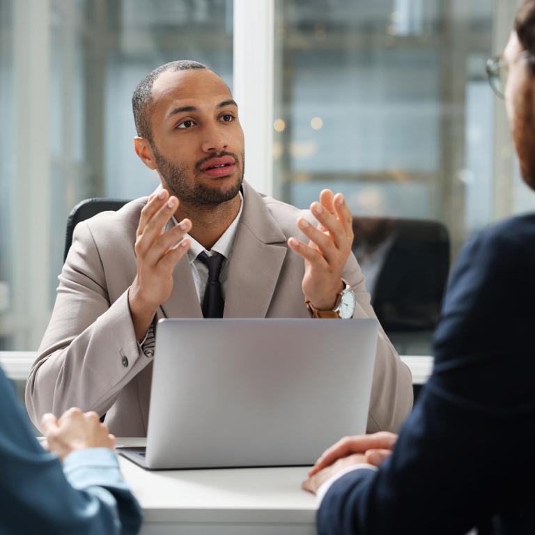 A man in a suit engages in conversation with two individuals in a professional setting.