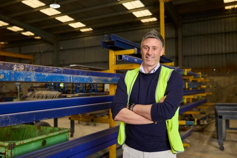 A man stands confidently in a factory, arms crossed, showcasing a sense of authority and professionalism in his environment.